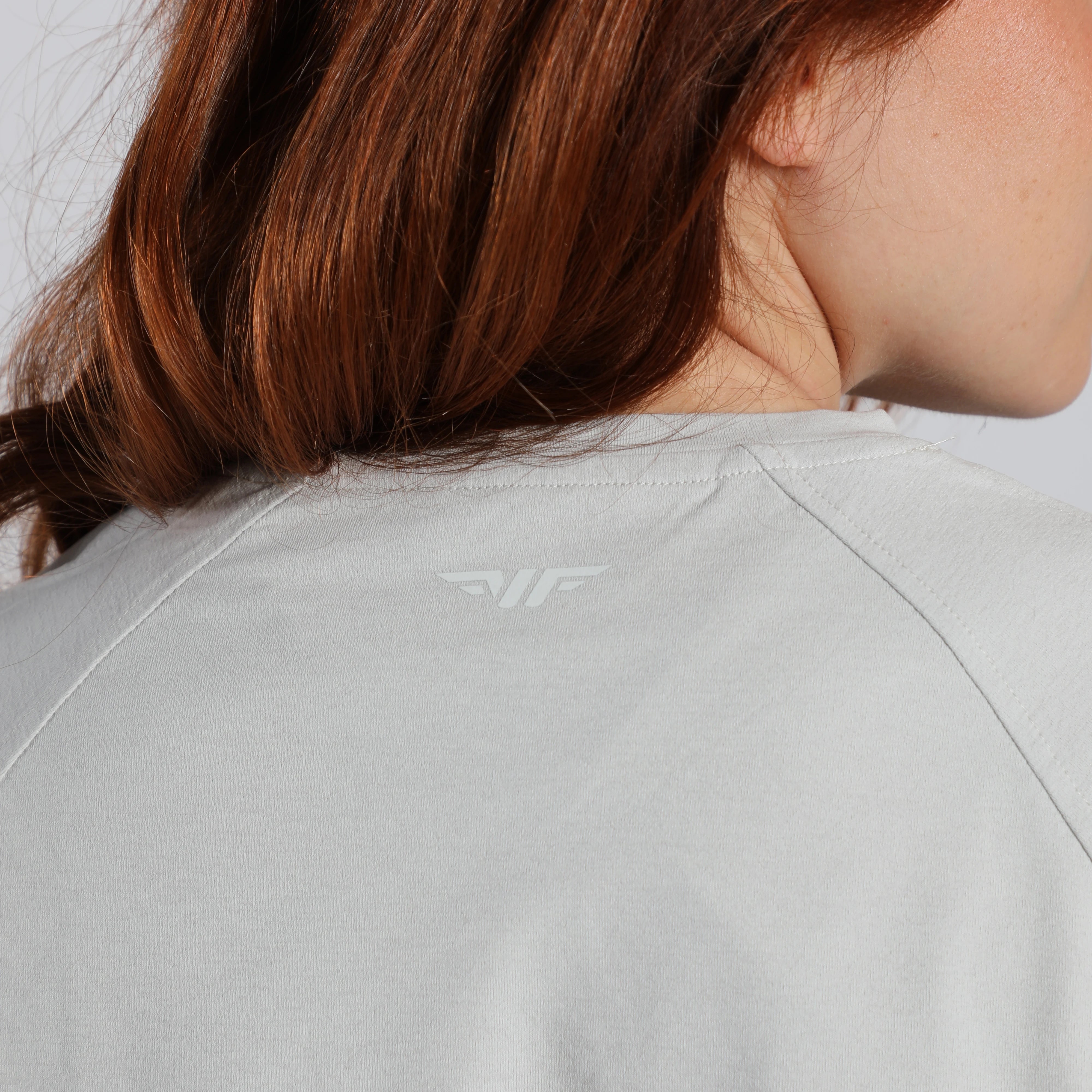Person wearing a light gray jacket with a brand logo on the back