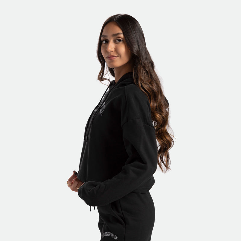 a fit woman stand at right and wearing   matching set black hoodie and pants 