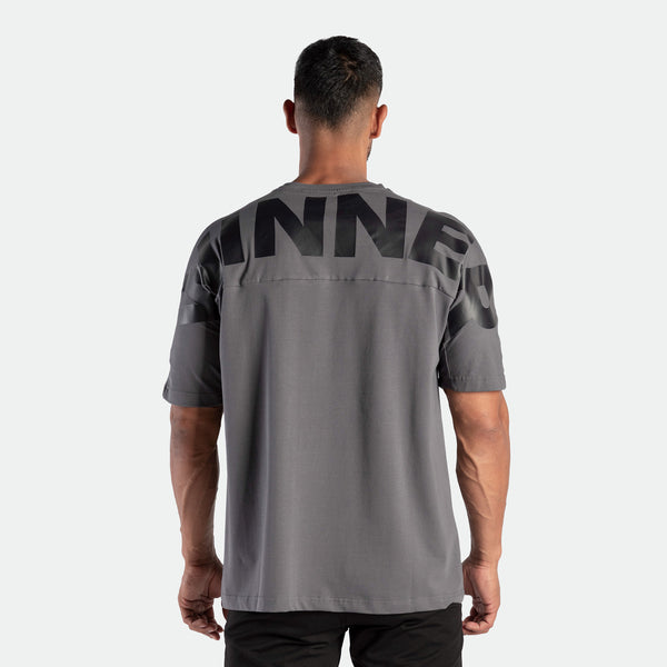Man wearing a gray t-shirt with large black letters across the back, standing 