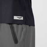 The image shows a close-up of a person wearing a dark blue shirt with a small logo above the hem and gray pants featuring a black zipper on the pocket.