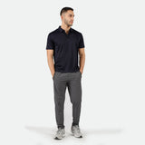 a fit man look at right and the two hands in pocket, he wearing t-shirt polo black and pants grey ,plus the shoes
