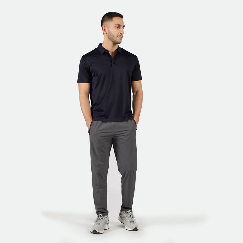 a fit man look at right and the two hands in pocket, he wearing t-shirt polo black and pants grey ,plus the shoes