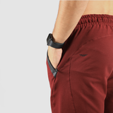 Close-up of a person wearing maroon athletic shorts with a hand in the black zippered pocket. A smart watch is visible on the wrist, against a white background.