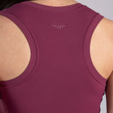 Close-up back view of a woman wearing a sleeveless athletic tank top in a muted berry/plum color, with ribbed neckline and shoulder cutouts and a subtle winged logo centered above the upper back.