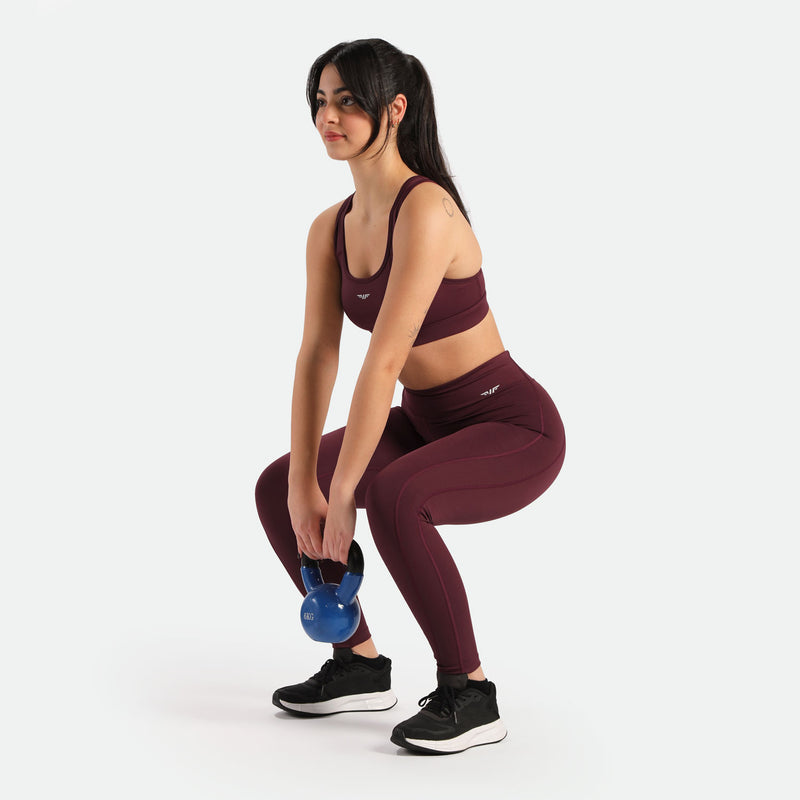 A woman wearing a red bra and leggings, with the same white Winnerforce logo but in a different direction, is squatting