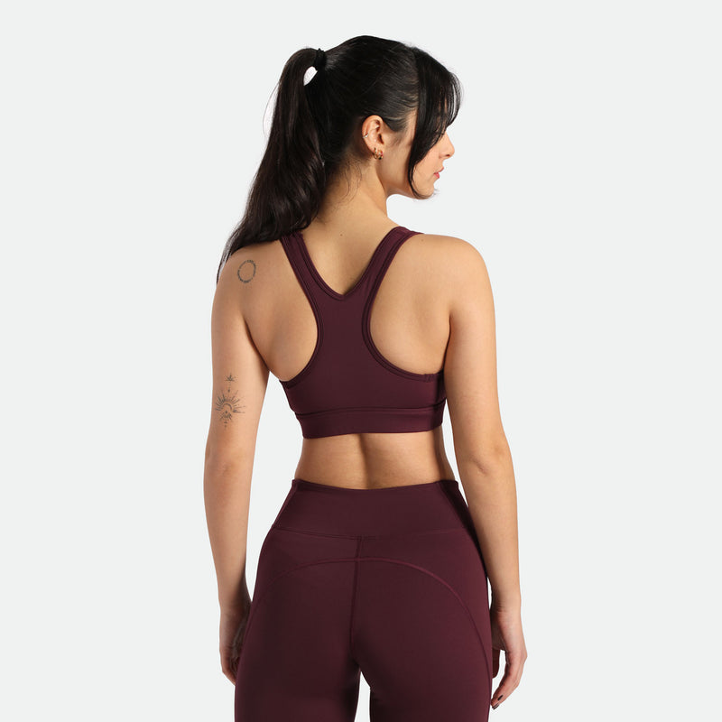 A woman wearing a burgundy sports bra and matching leggings stands with her back to the camera