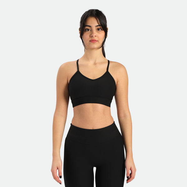 A fit young woman with dark hair in a ponytail wears black sports bra and matching leggings ,its is have same logo 