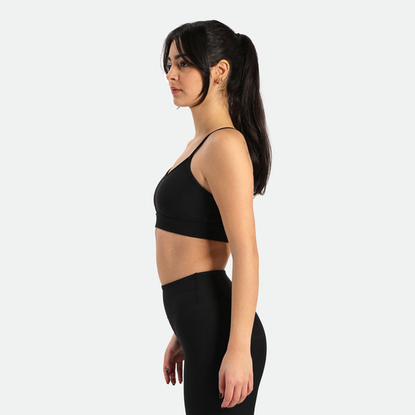 Young slim woman with dark hair tied in a ponytail wearing a sports bra and teal leggings black