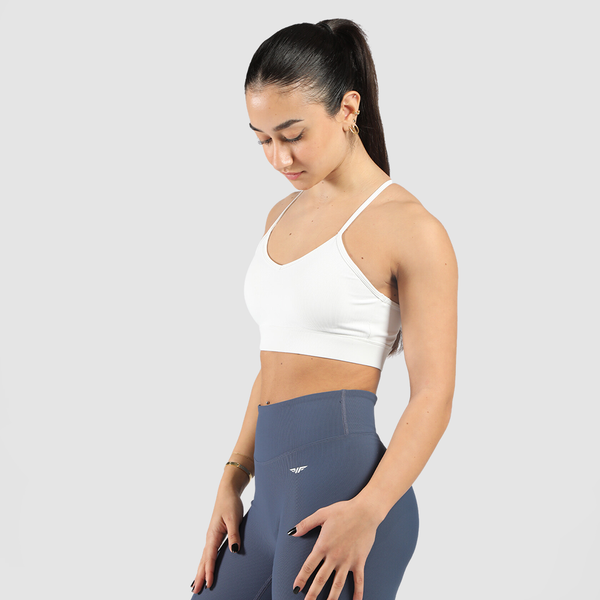 Woman wearing a white sports bra with a stylish cutout design, and dark blue high-waisted leggings, standing in front of a neutral background.