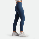 a fit woman stand at right and wearing legging ensign blue ,plus the shoes white 
