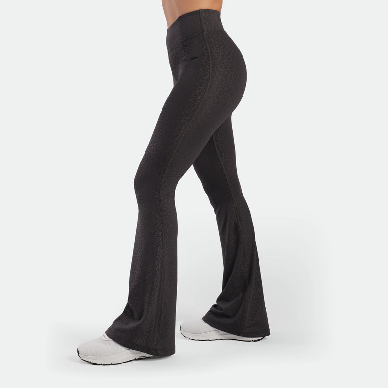 a fit woman stand at right and wearing flared legging graphite grey leopard  with shoes 