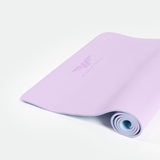 A rolled lavender yoga mat with a subtle logo, unrolling against a light background. The scene conveys a calm, inviting atmosphere for relaxation.