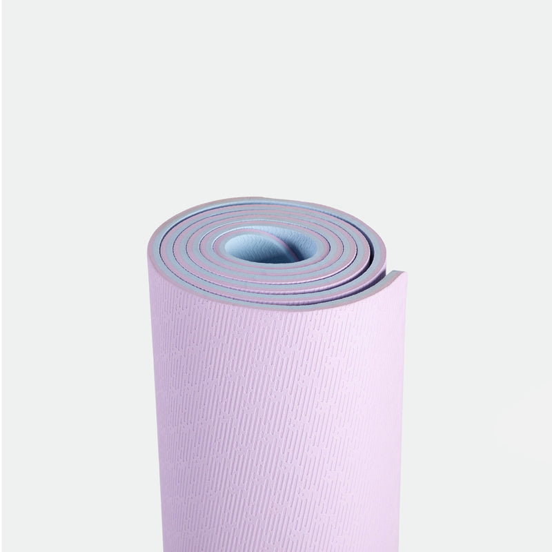 A neatly rolled yoga mat in pastel pink and blue against a plain white background. It has a subtle textured pattern, conveying simplicity and calmness.
