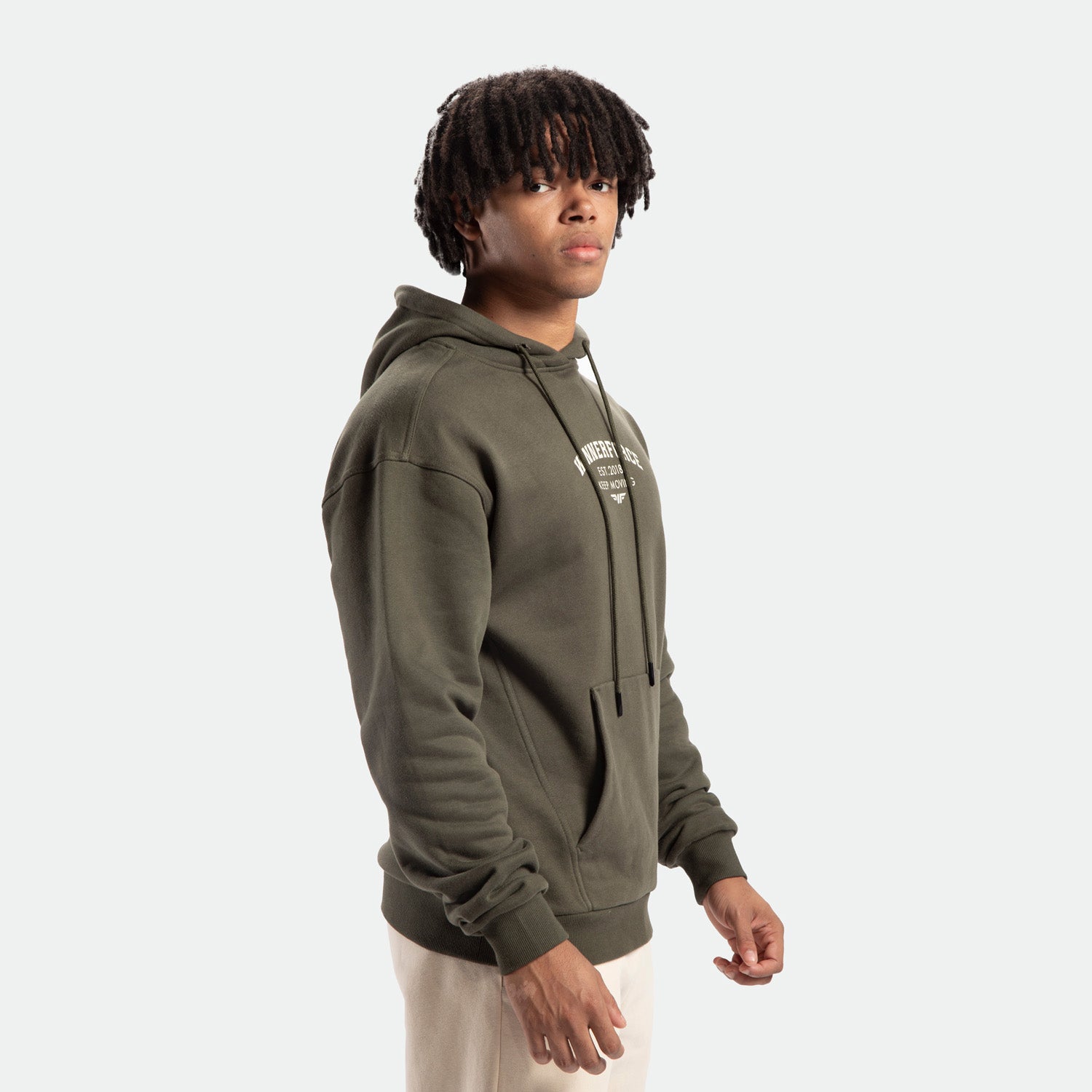 a fit man stand at right and wearing hoodie forest night green with pants beige 