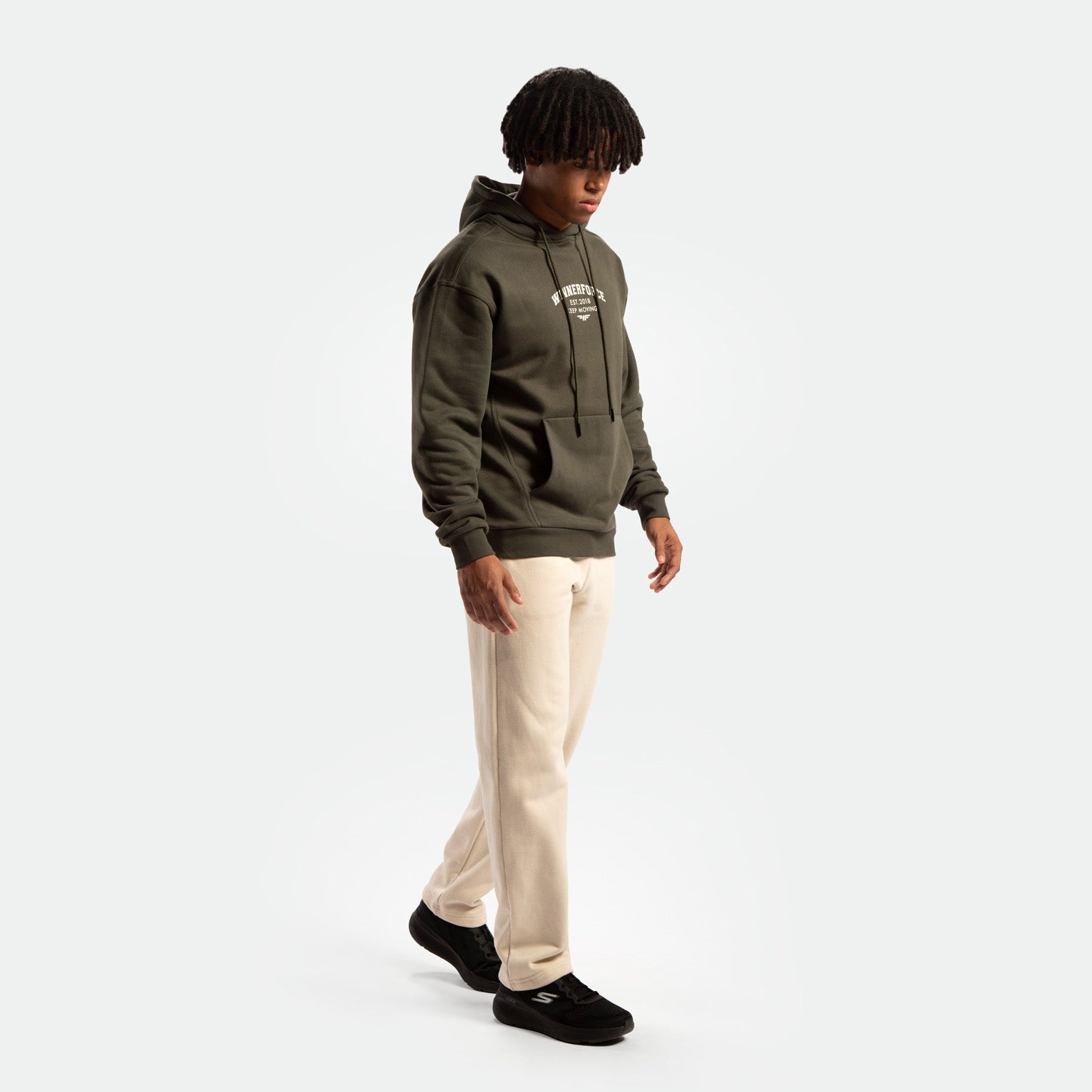 a fit man stand at right and wearing  hoodie forest night green and pants green ,plus the shoes black 