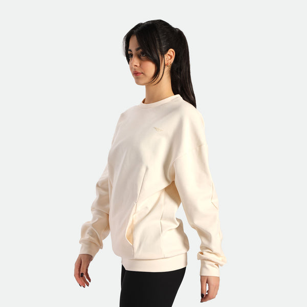 A person wearing a light beige oversized sweatshirt, paired with black leggings, striking a casual pose against a plain background.