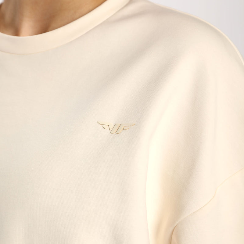 Close-up of a model wearing a soft beige sweatshirt featuring a subtle golden logo on the chest.