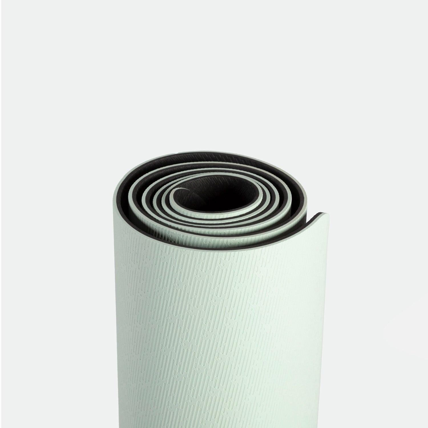 Rolled up light green yoga mat with subtle textured pattern on a plain white background. The mat’s spiral shape conveys simplicity and readiness.