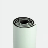 Rolled up light green yoga mat with subtle textured pattern on a plain white background. The mat’s spiral shape conveys simplicity and readiness.