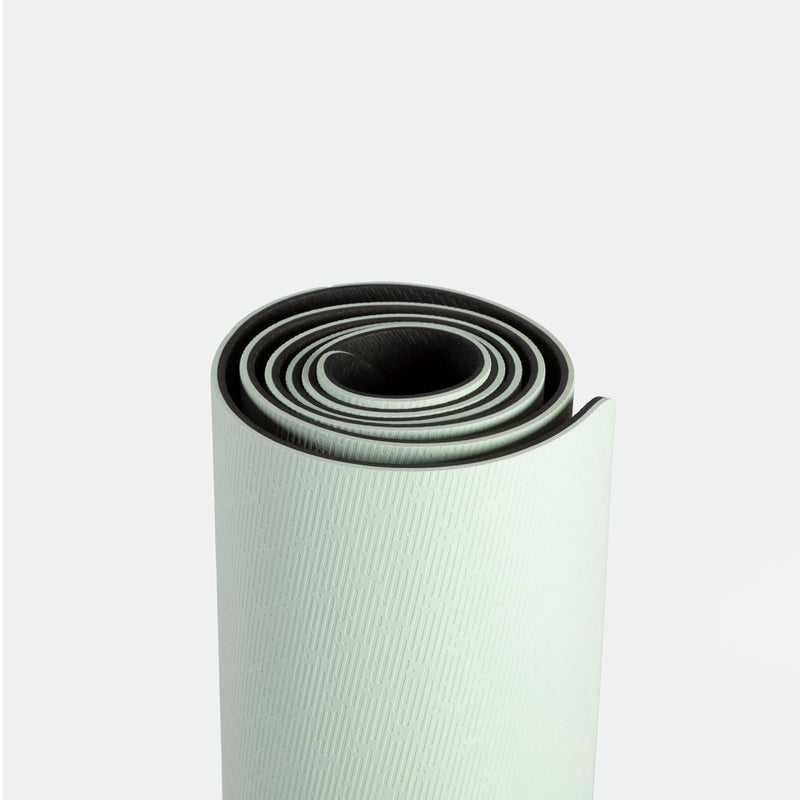 Rolled up light green yoga mat with subtle textured pattern on a plain white background. The mat’s spiral shape conveys simplicity and readiness.