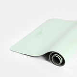 A light green yoga mat partially rolled up on a white surface, displaying a subtle logo and texture, conveying a fresh, minimalist, and calm tone.