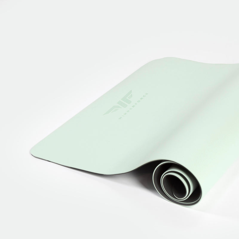 A light green yoga mat partially rolled up on a white surface, displaying a subtle logo and texture, conveying a fresh, minimalist, and calm tone.