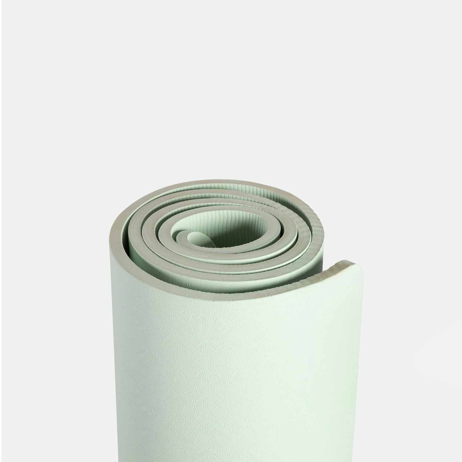 A neatly rolled light green yoga mat on a plain white background, highlighting its textured surface and clean edges, conveying simplicity and calm.