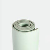 A neatly rolled light green yoga mat on a plain white background, highlighting its textured surface and clean edges, conveying simplicity and calm.