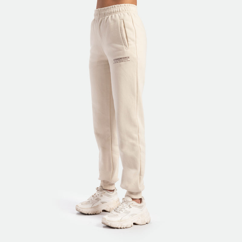 a fit woman stand at right  and she wearing jogger pant beige with white shoes ,plus the background is light grey 