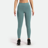 a fit woman wearing legging green with logo white on front ,shoes black ,the background is light grey