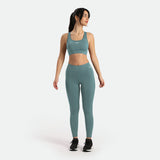 a fit woman look at right and wearing  matching bra with legging  goblin blue  ,logo white ,shoes black ,the background is light grey 