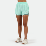 a fit woman wearing  beach class blue short 2 in1 with shoes white ,plus the background is light grey 
