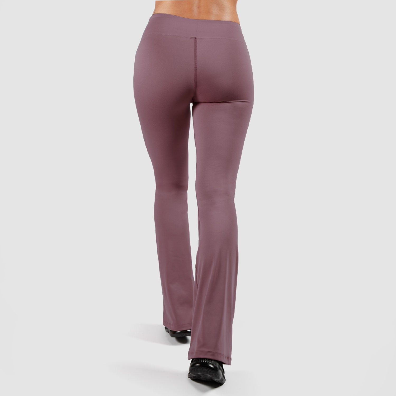 a back view for woman wearing flared legging with shoes black ,plus the background is light grey 