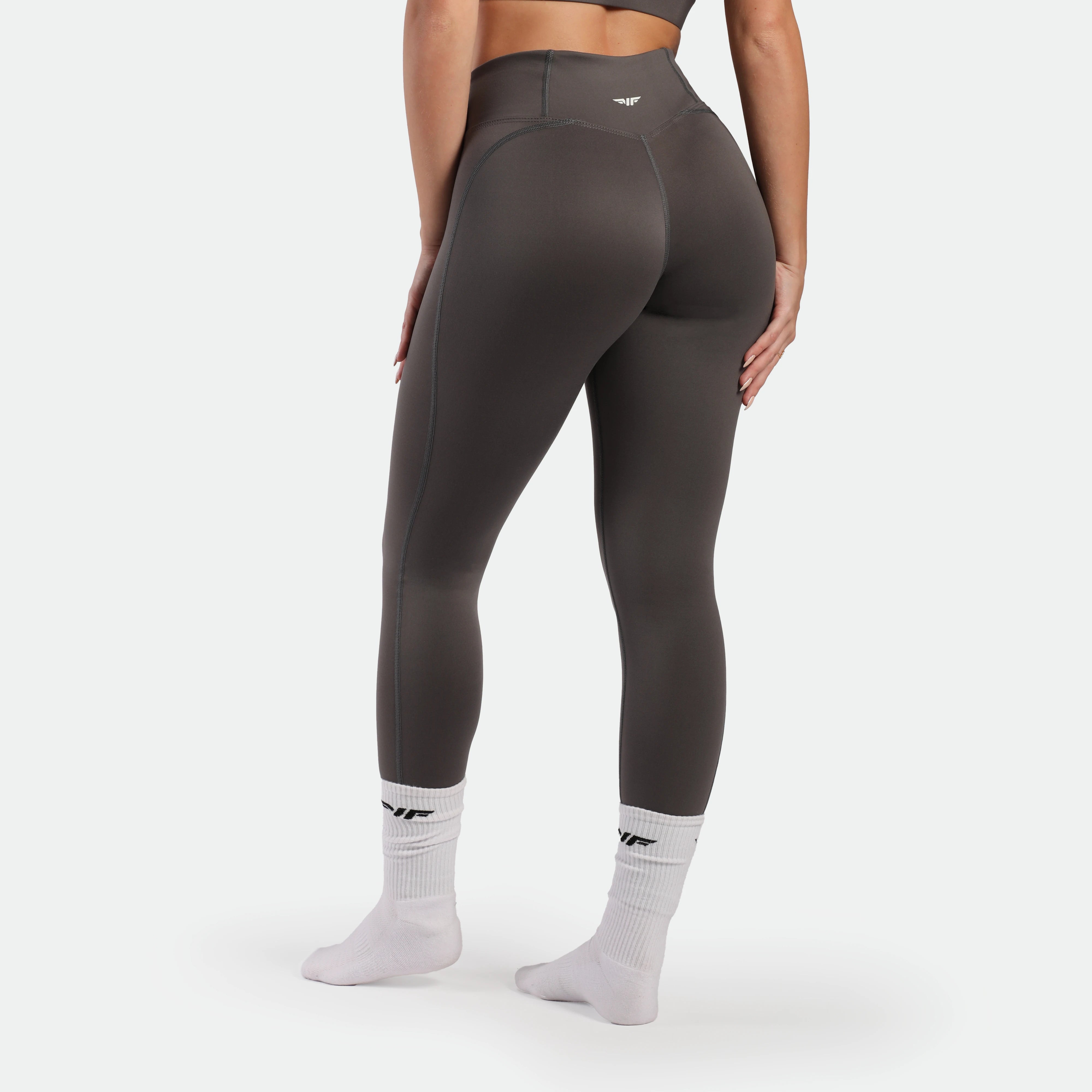Person wearing dark gray leggings with a logo on a white background