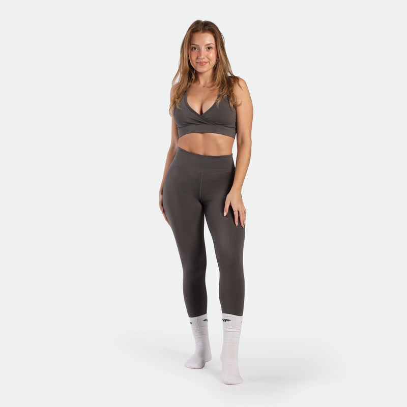 Woman wearing a gray sports bra and leggings set on a white background