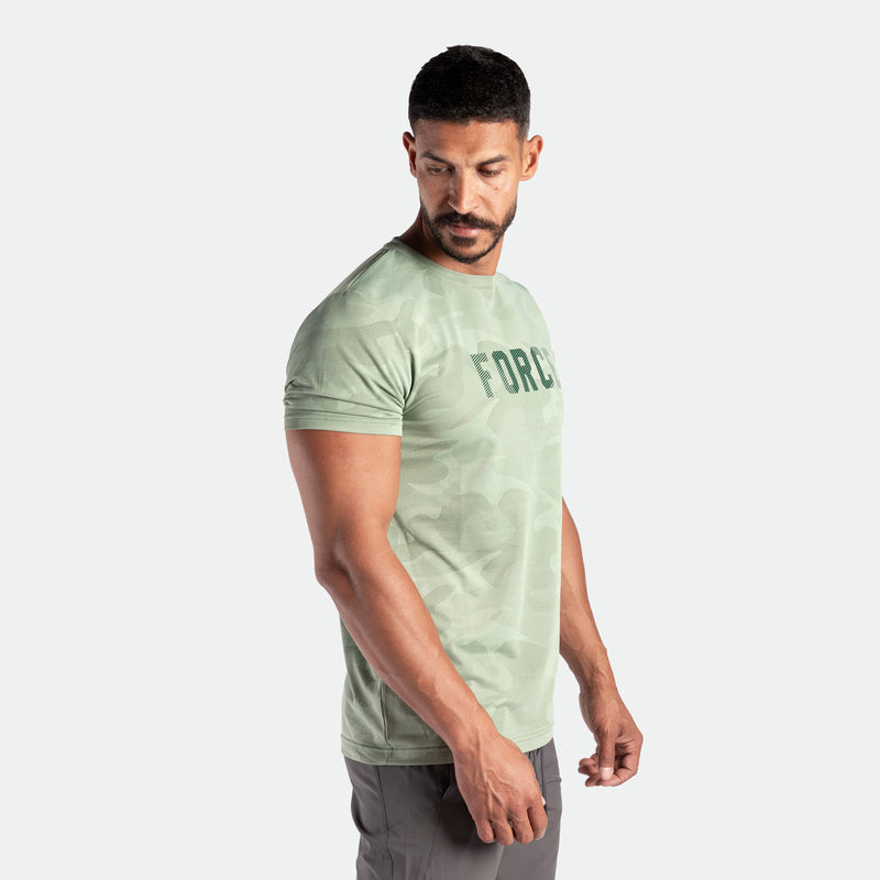 a fit man stand at right and wearing  camo t-shirt green by with logo ,and pants grey 