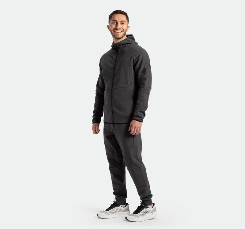 a fit man stand with pose and smile ,he wearing  matching color grey ebony jacket and pants with shoes sports 