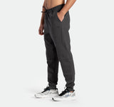 a fit man stand at right and wearing  pants grey ebony with shoes sports 