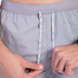 Close-up of a person adjusting drawstrings on light gray athletic shorts. The drawstrings have "WINNERFORCE" printed in white. Relaxed and casual tone.