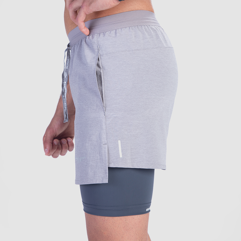 A person wearing light gray athletic shorts with a drawstring and dark gray compression shorts underneath. The style is sporty and casual.