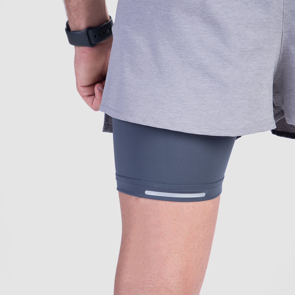 A person wearing gray athletic shorts with navy compression layers underneath. A black smartwatch is visible on the left wrist, conveying a sporty tone.