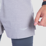 Close-up of a person's hand wearing a fitness tracker, next to gray athletic shorts and dark leggings. The logo is visible on the shorts. The mood is sporty.