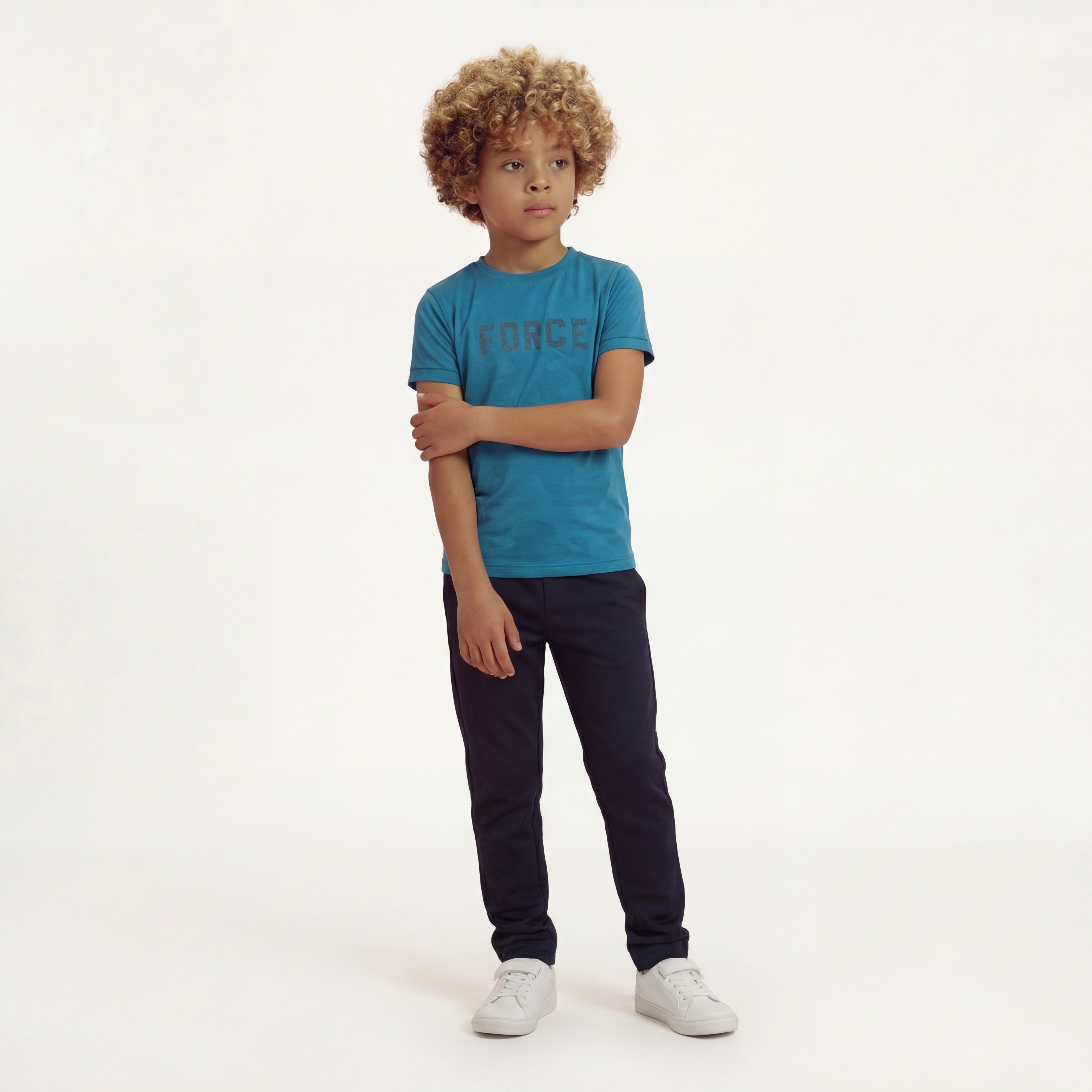 A boy posing and wearing a regular fit saxony blue camo t-shirt with the word FORCE in big on it. He is also wearing navy pants and white shoes.