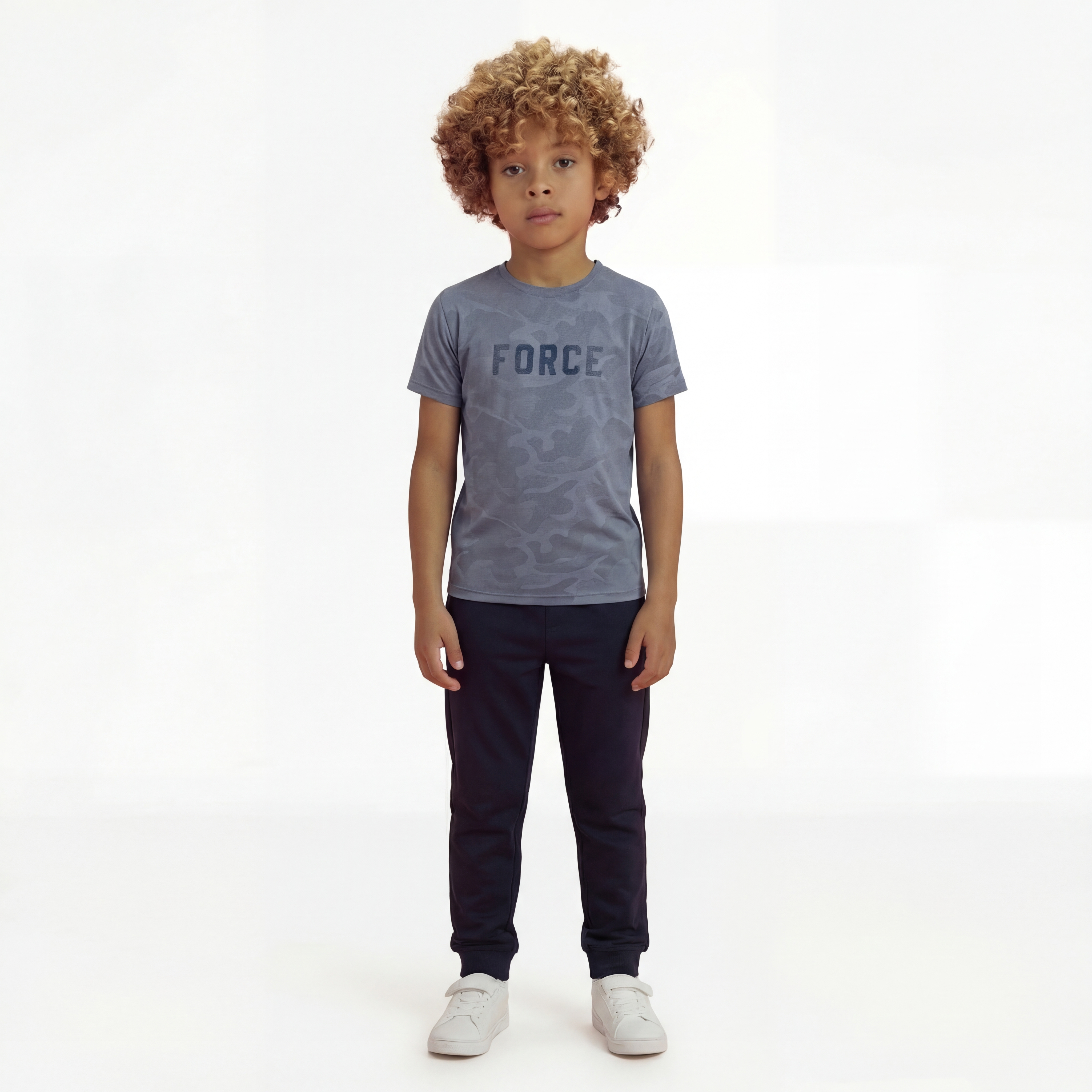 A boy posing and wearing a regular fit vintage indigo camo t-shirt with the word FORCE in big on it. He is also wearing navy pants and white shoes.