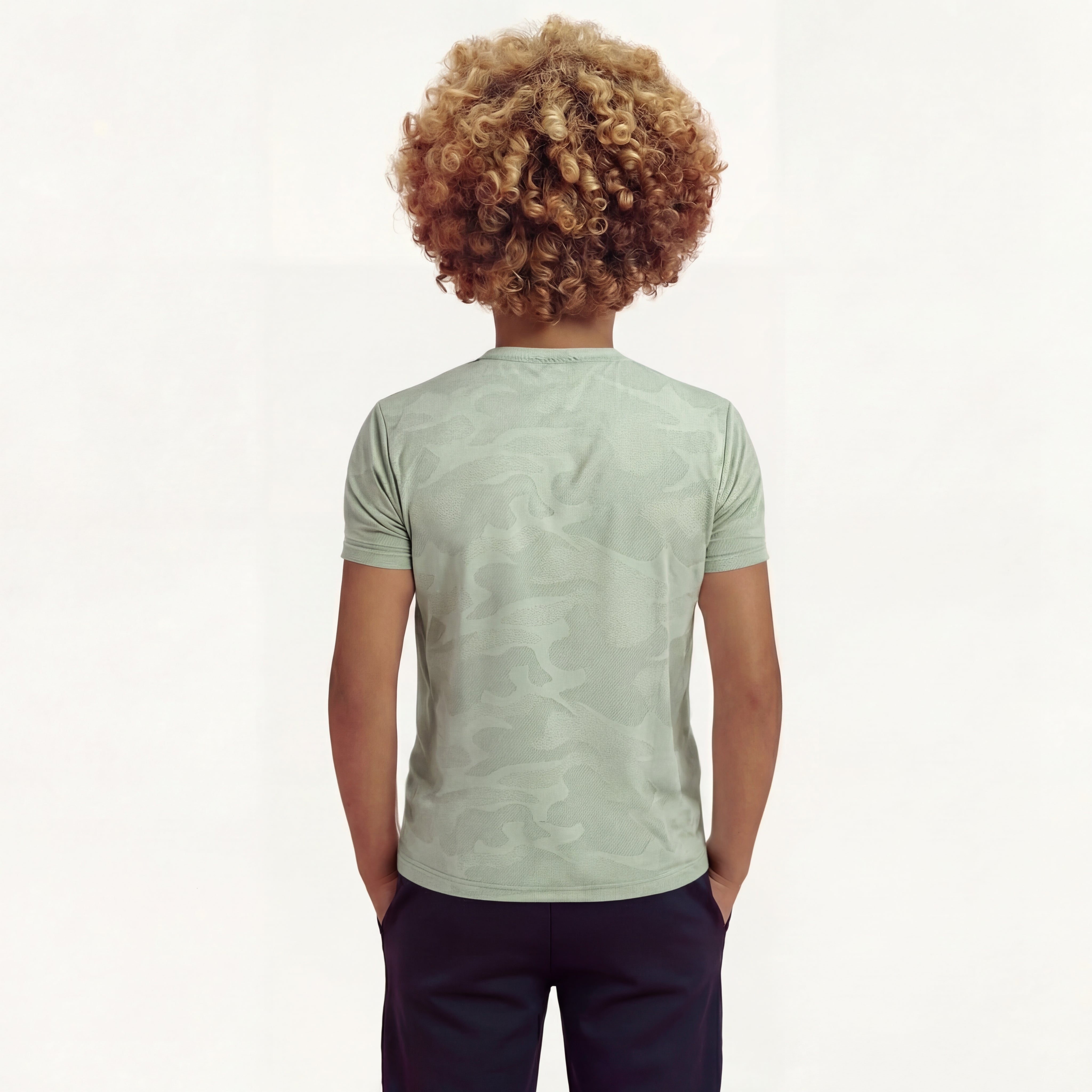Back close-up view of a boy wearing a regular fit camo t-shirt in the color green bay. He is also wearing navy pants.
