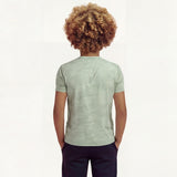 Back close-up view of a boy wearing a regular fit camo t-shirt in the color green bay. He is also wearing navy pants.