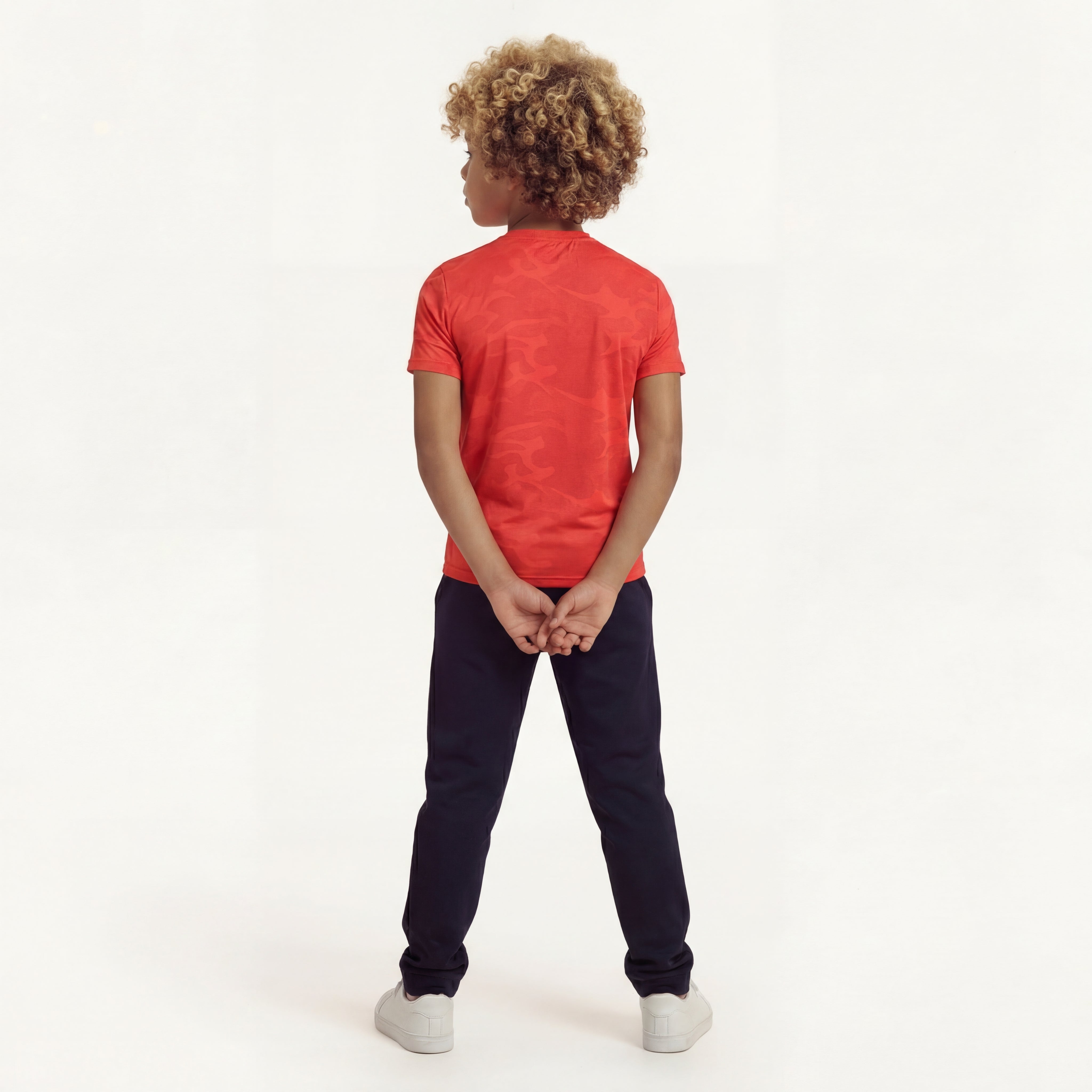 Back view of a boy posing and wearing a regular fit camo t-shirt in the color high risk red. He is also wearing navy pants and white shoes.