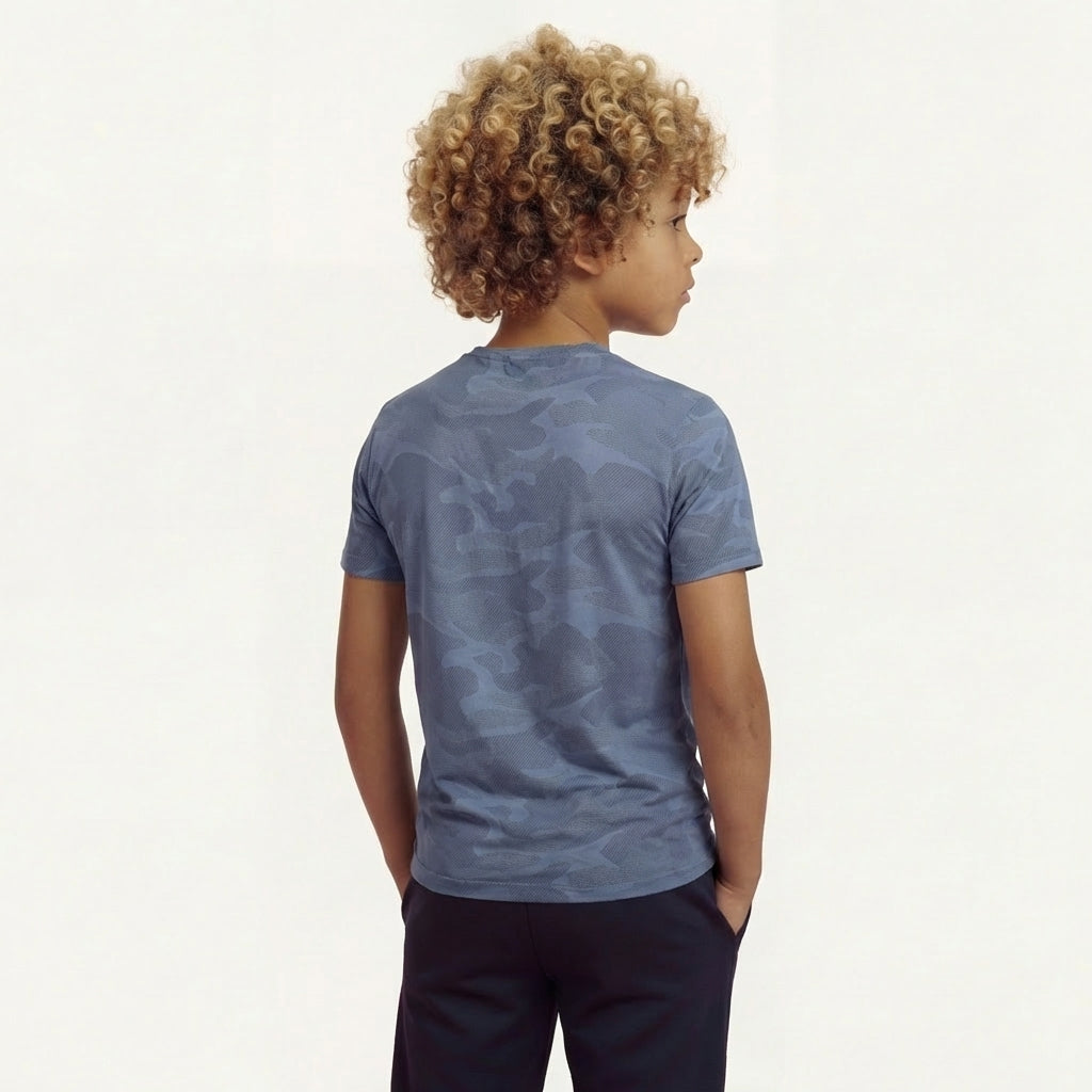 Back view of a boy posing, his hands in his pockets and wearing a regular fit vintage indigo camo t-shirt. He is also wearing navy pants.