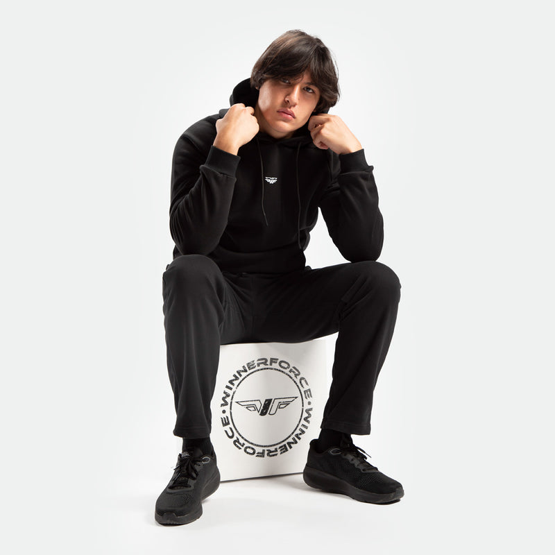 a fit man wearing matching color set black ,hoodie and pants ,plus he sits  on block white with logo winnerforce 