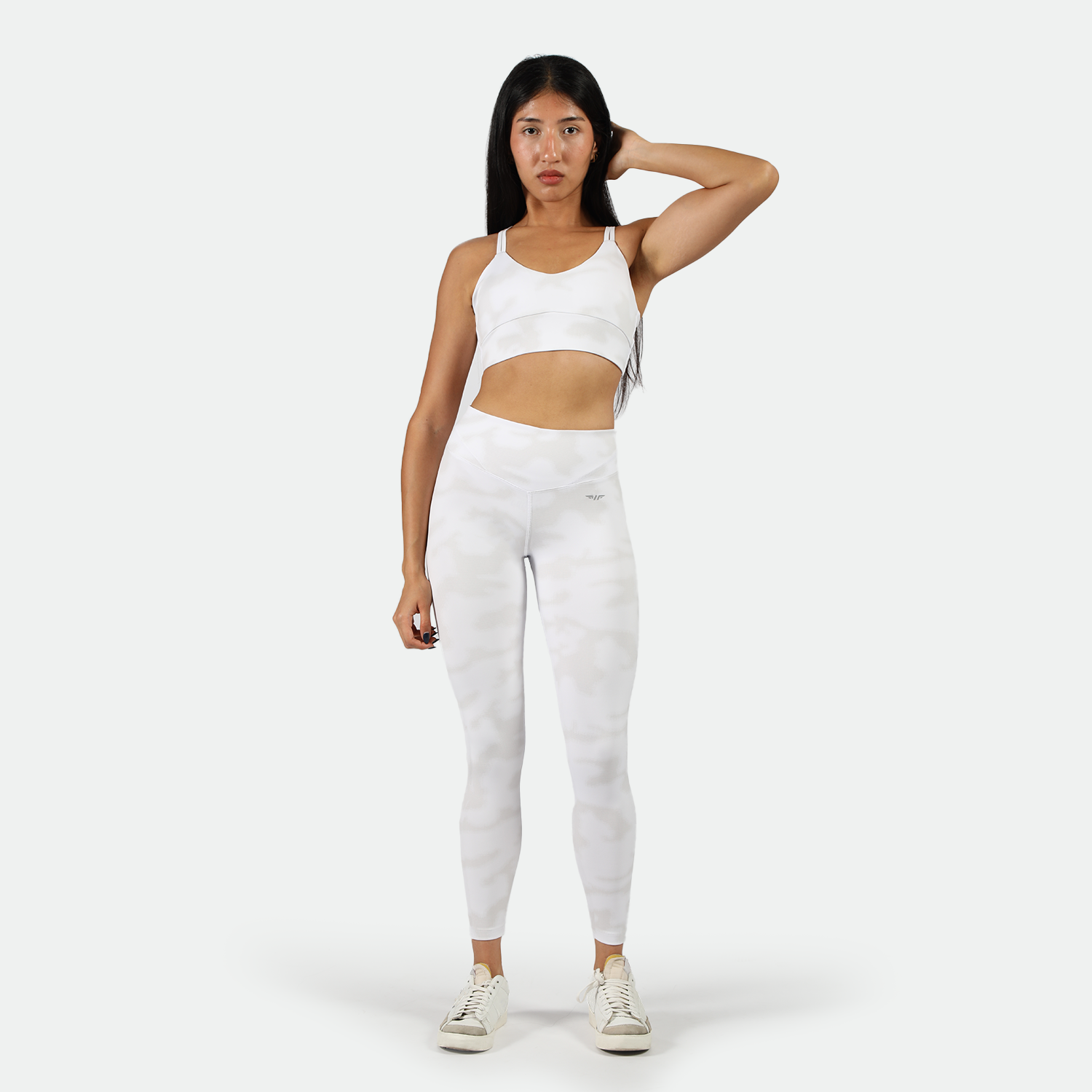 a woman look at the camera and stand with pose, she wearing matching bra and legging illuminated white with shoes ,plus the background is light grey 